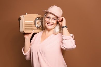 Beautiful mature woman listening to radio against color background