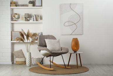 Photo of Soft rocking chair with pillow on rug near wall in room. Interior design