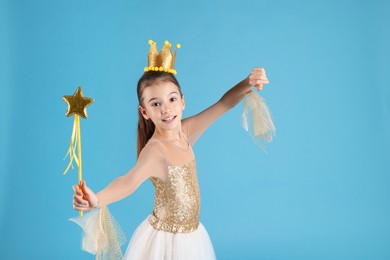 Cute girl in fairy dress with golden crown and magic wand on light blue background. Little princess