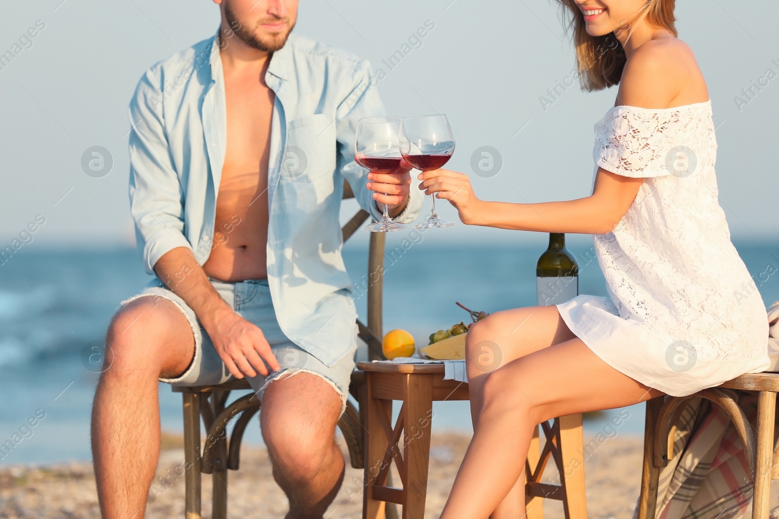 Photo of Young couple with glasses of wine having romantic dinner on beach