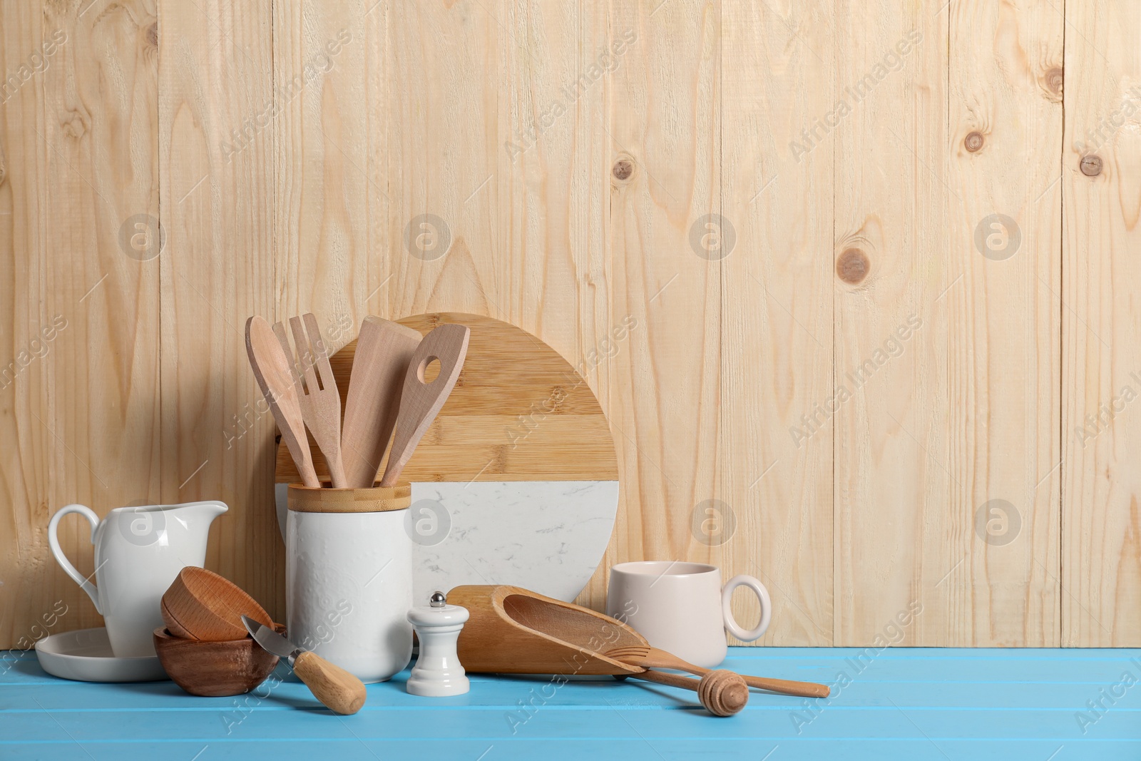 Photo of Set of different kitchen utensils on light blue table against wooden background, space for text