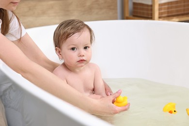 Mother bathing her cute little baby in tub at home