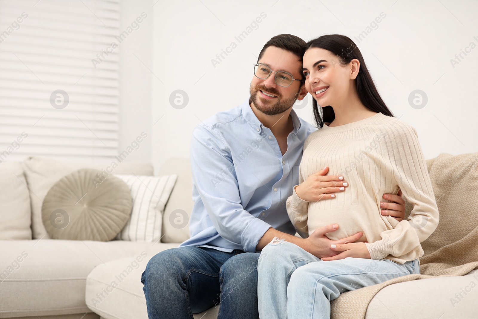 Photo of Happy pregnant woman with her husband on sofa at home