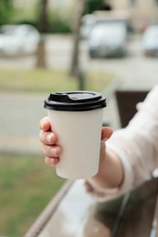 Photo of Woman holding paper takeaway cup at table outdoors, closeup. Coffee to go