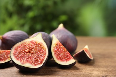 Whole and cut ripe figs on wooden table against blurred green background, closeup. Space for text