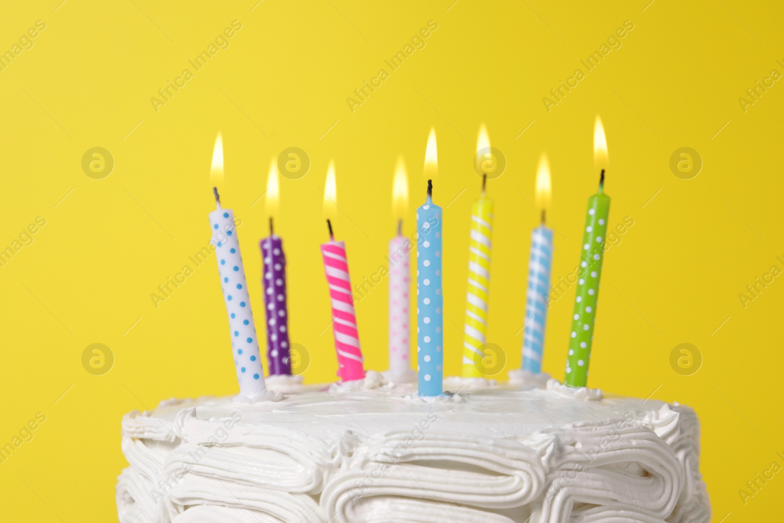 Photo of Delicious cake with cream and burning candles on yellow background, closeup