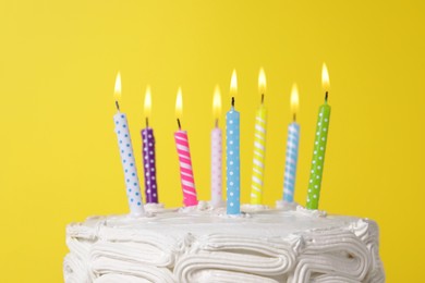 Delicious cake with cream and burning candles on yellow background, closeup