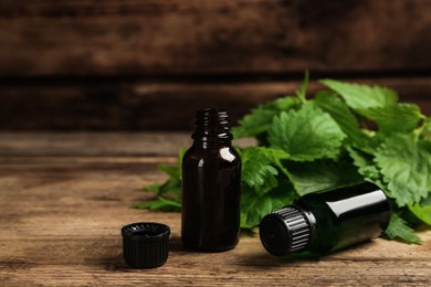 Photo of Glass bottles of nettle oil with leaves on wooden table