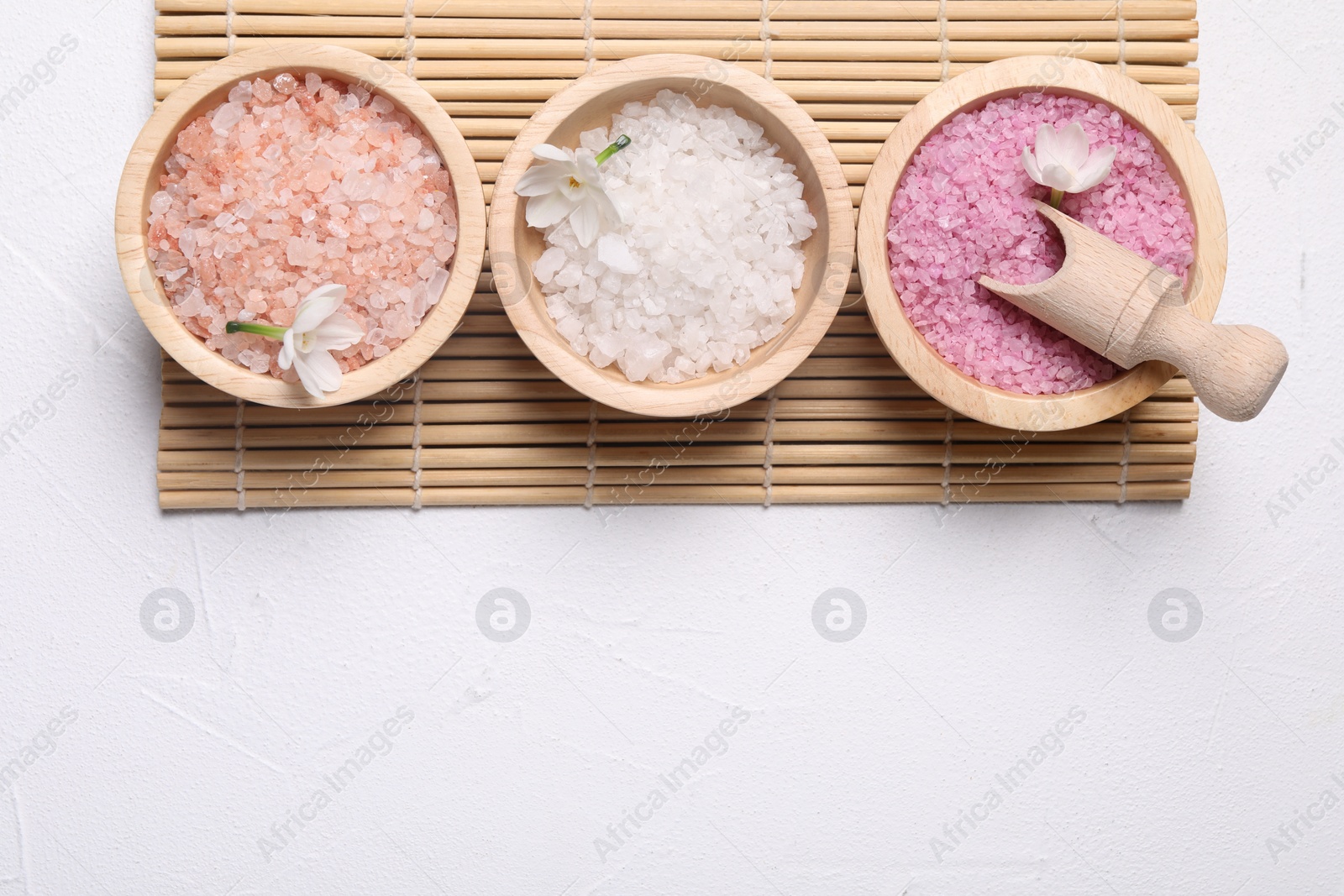 Photo of Different types of sea salt and flowers on light table, flat lay. Spa products