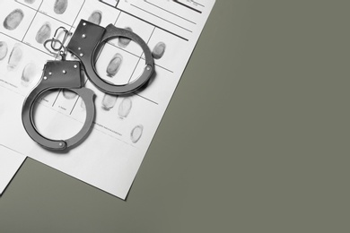 Photo of Police handcuffs and criminal fingerprints card on grey background. Space for text