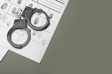 Police handcuffs and criminal fingerprints card on grey background. Space for text