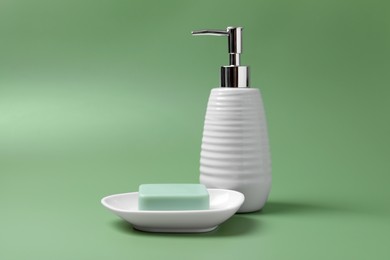 Photo of Soap bar and bottle dispenser on green background