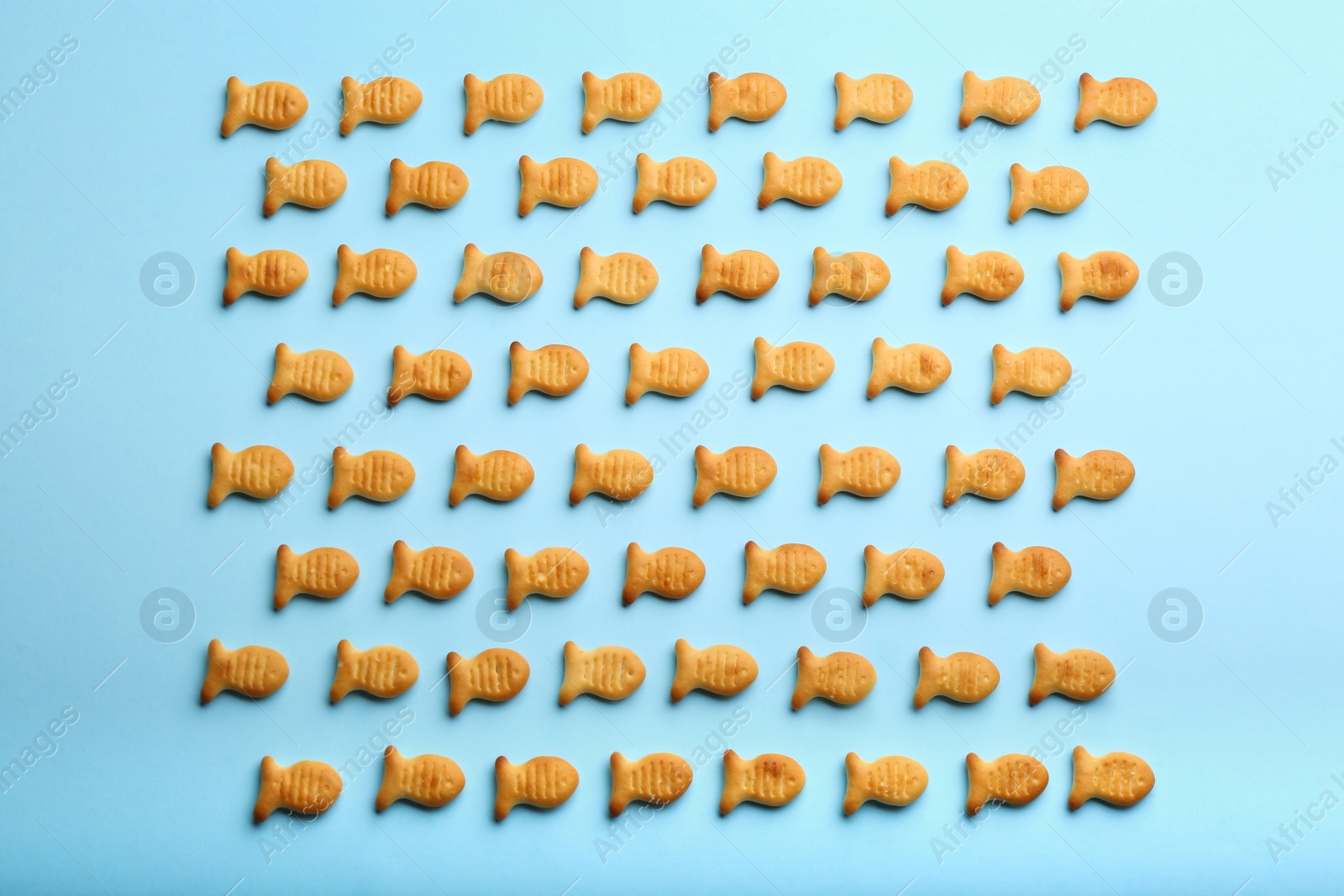 Photo of Delicious goldfish crackers on light blue background, flat lay