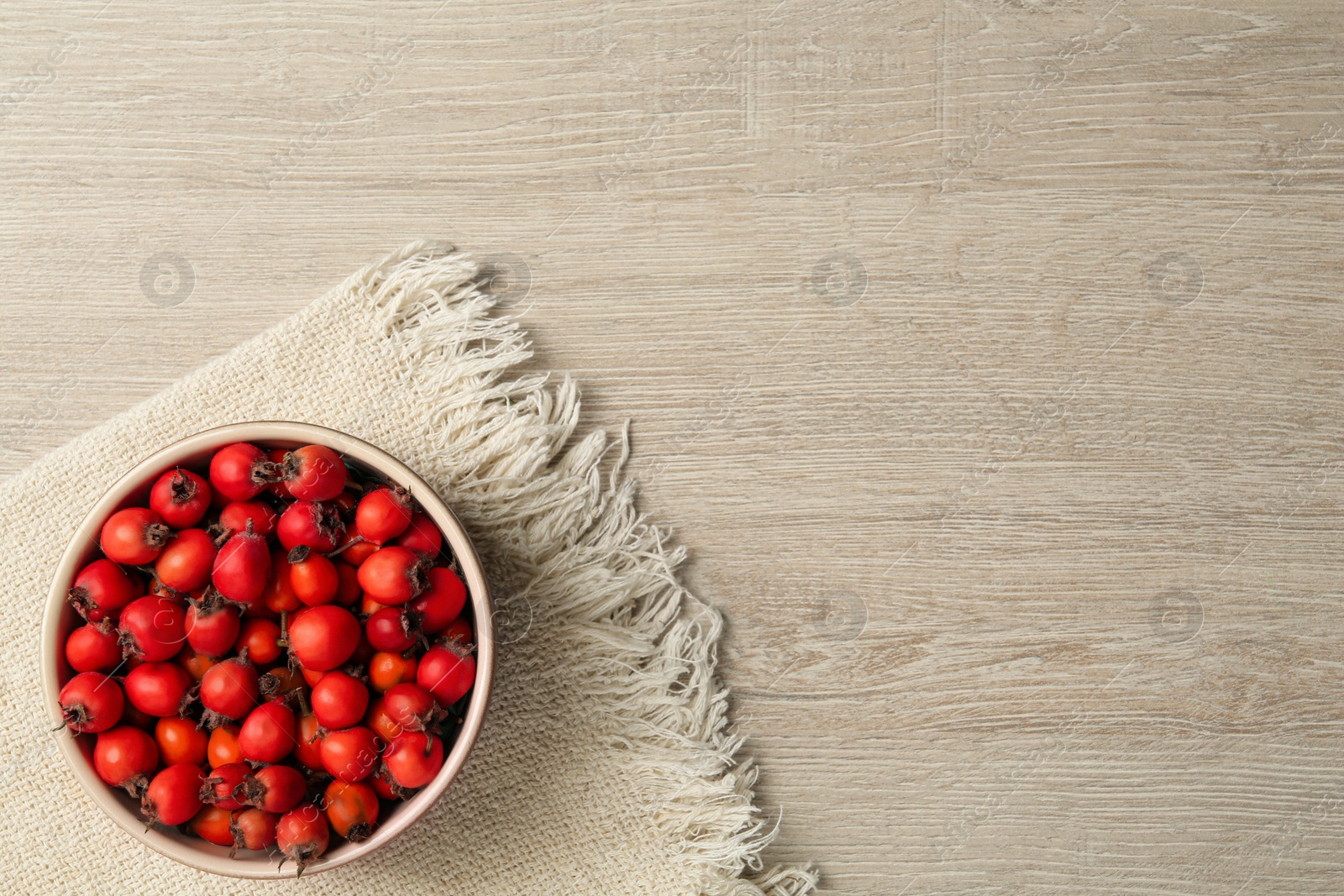 Photo of Ripe rose hip berries in bowl on wooden table, top view. Space for text