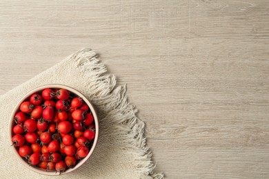 Ripe rose hip berries in bowl on wooden table, top view. Space for text