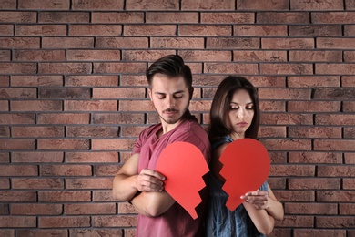 Photo of Young couple with torn paper heart near brick wall. Relationship problems