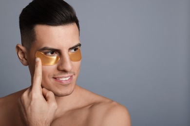 Photo of Man applying golden under eye patch on grey background. Space for text