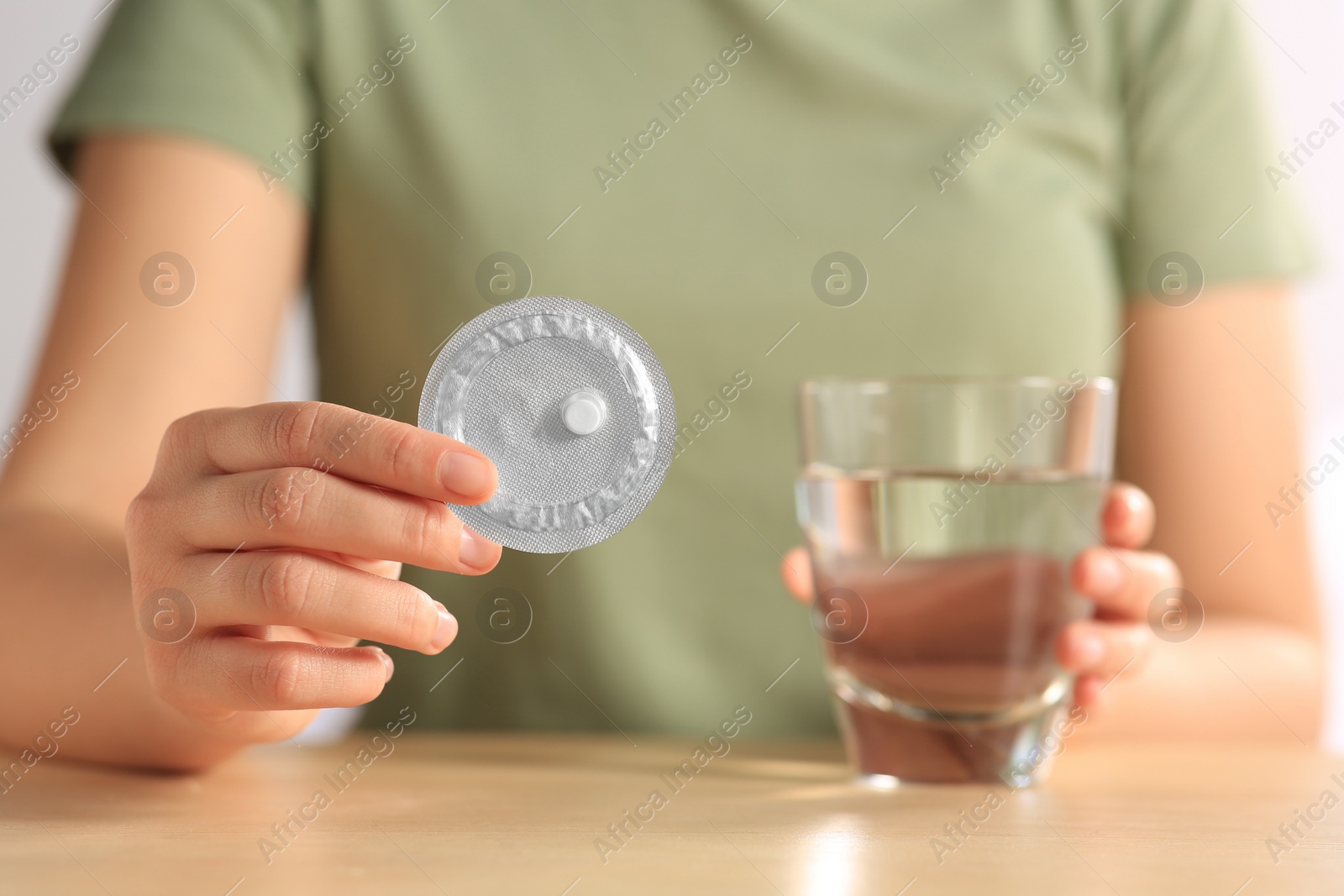 Photo of Woman taking emergency contraception pill at wooden table indoors, focus on hand