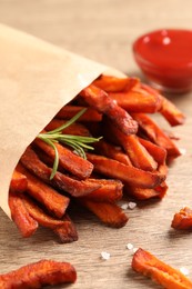Paper bag with tasty sweet potato fries and sauce on wooden table, closeup