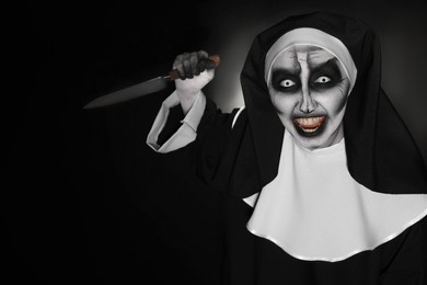 Scary devilish nun with knife on black background, space for text. Halloween party look