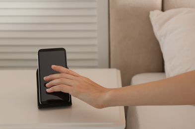 Woman taking smartphone from wireless charger in bedroom, closeup