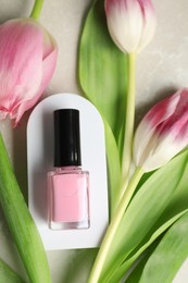 Flat lay composition with bright nail polish in bottle and tulip flowers on light textured table