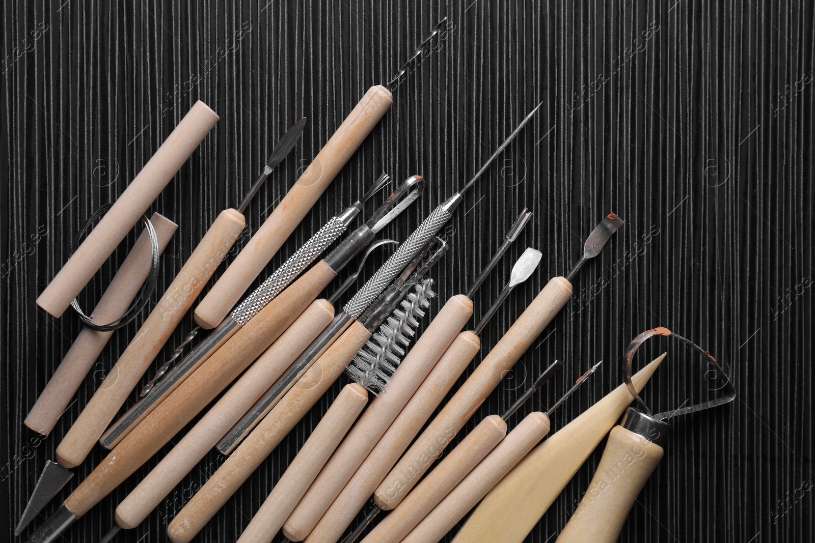 Photo of Clay and set of modeling tools on dark gray wooden table, flat lay