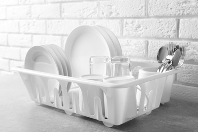 Photo of Dish drainer with clean plates on table near brick wall