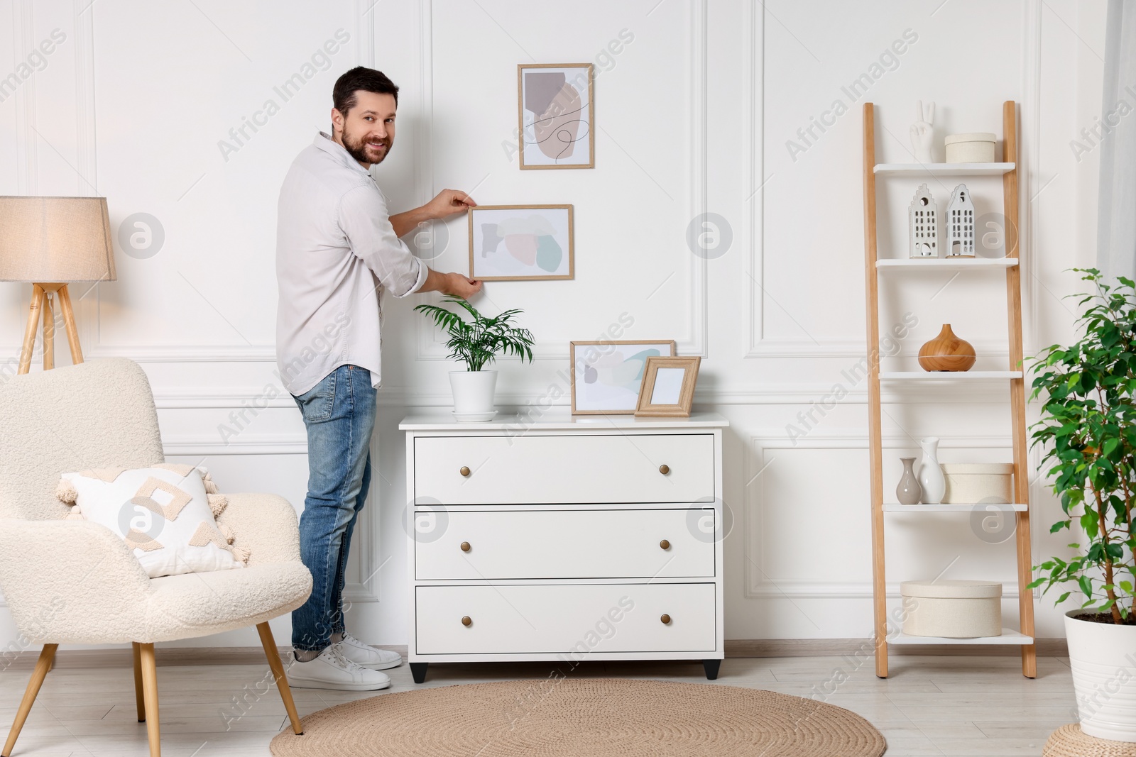 Photo of Man hanging picture frame on white wall at home