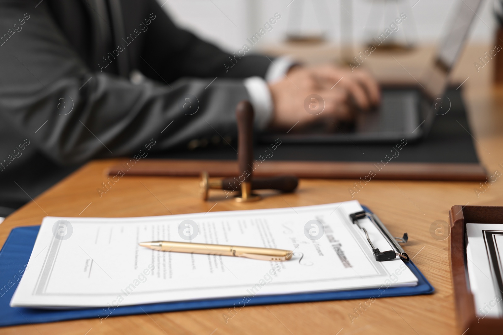 Photo of Notary working with laptop at wooden table in office, focus on clipboard and pen