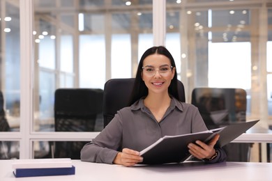 Photo of Smiling woman working at table in office. Lawyer, businesswoman, accountant or manager