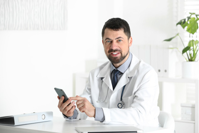 Male doctor with smartphone at table in office