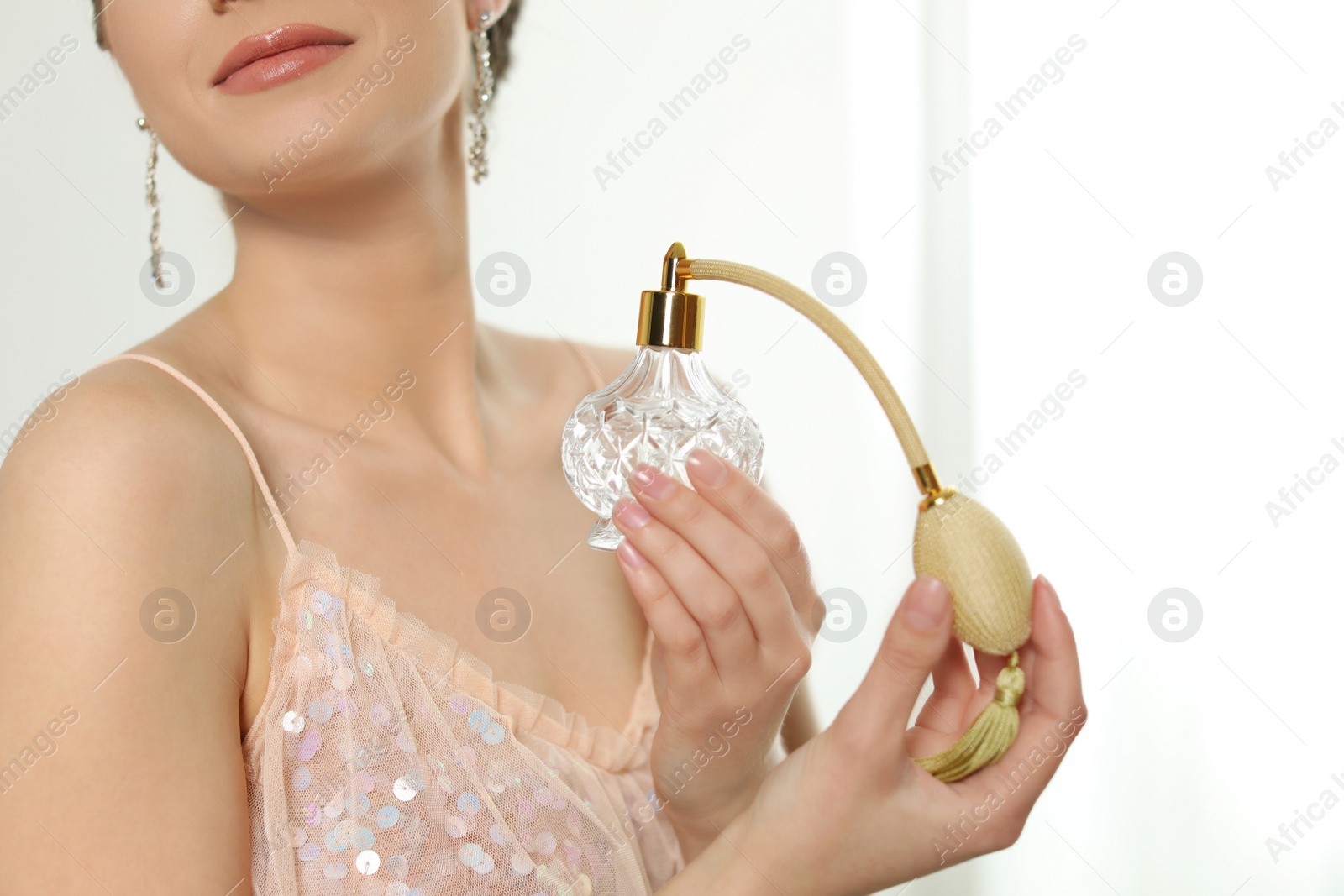 Photo of Young woman applying perfume against blurred background, closeup. Space for text