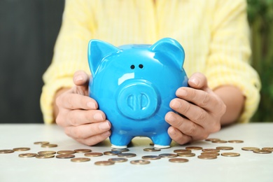 Photo of Woman with piggy bank and coins at light table, closeup