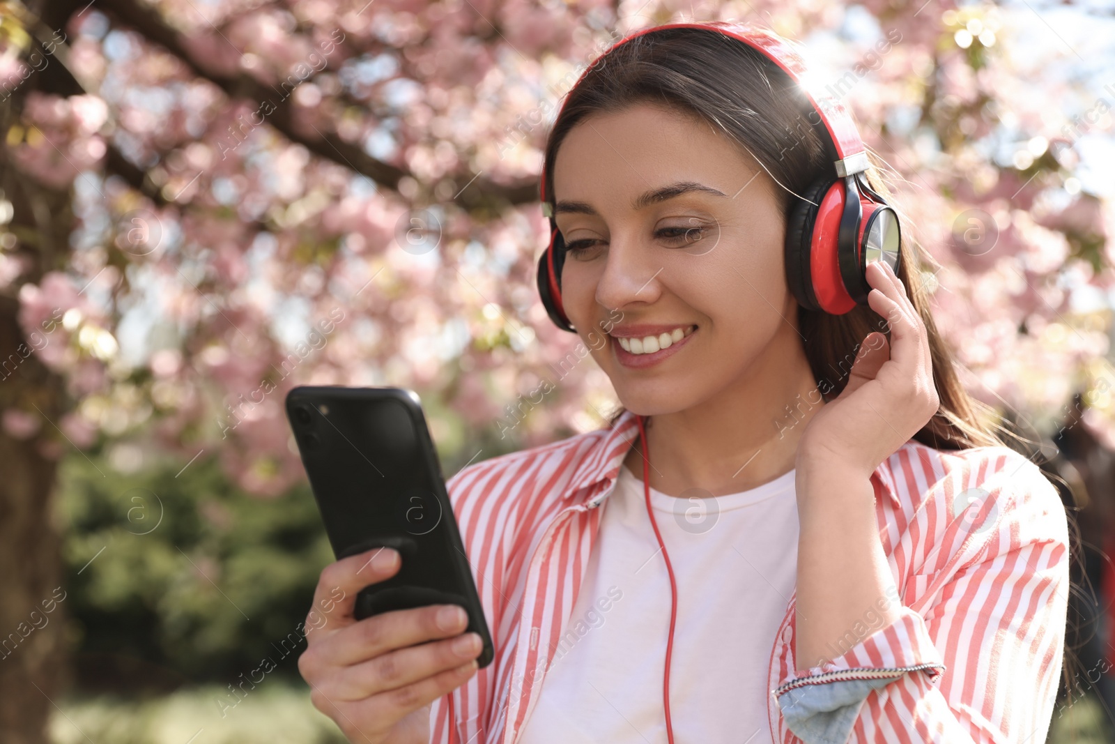 Photo of Young woman with smartphone and headphones listening to music outdoors