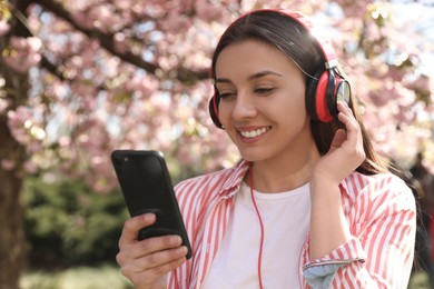 Young woman with smartphone and headphones listening to music outdoors
