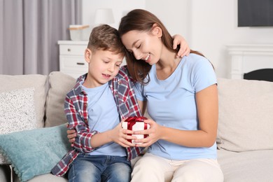 Photo of Little boy presenting his mother with gift on sofa at home