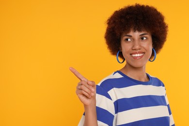 Photo of Happy young woman pointing at something on orange background. Space for text