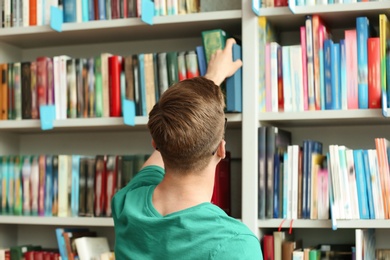 Photo of Young man taking book from shelving unit in library