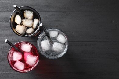 Glasses of different refreshing soda water with ice cubes and straws on black table, flat lay. Space for text