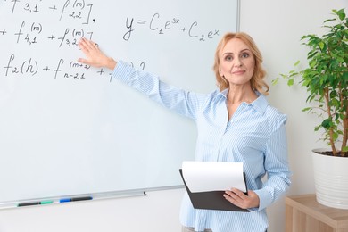 Photo of Professor with clipboard giving lecture near whiteboard in classroom