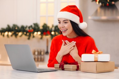 Photo of Celebrating Christmas online with exchanged by mail presents. Smiling woman thanking for gift during video call at home