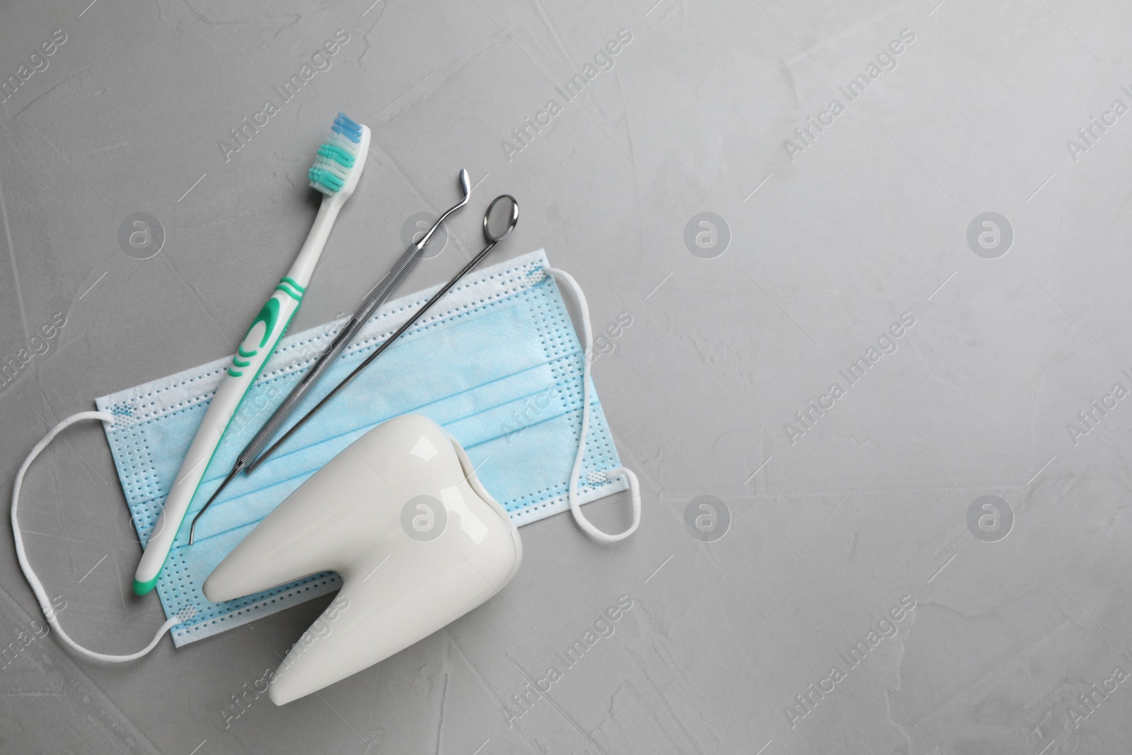 Photo of Tooth shaped holder, dentist's tools, toothbrush and face mask on grey table, flat lay. Space for text