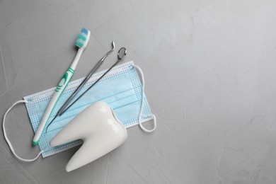 Tooth shaped holder, dentist's tools, toothbrush and face mask on grey table, flat lay. Space for text