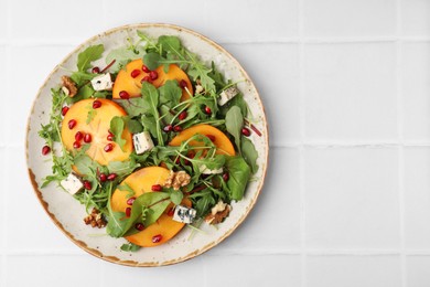 Tasty salad with persimmon, blue cheese, pomegranate and walnuts served on white tiled table, top view. Space for text