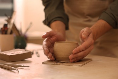 Photo of Clay crafting. Man making bowl at table, closeup