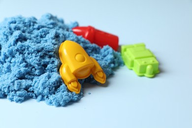 Photo of Bright kinetic sand and plastic toys on light blue background, space for text