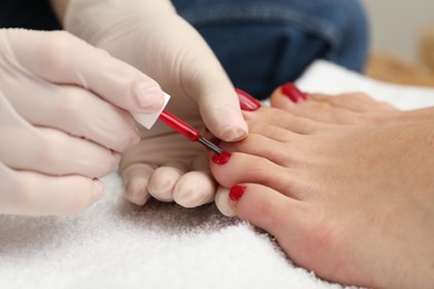 Photo of Pedicurist painting client`s toenails with red polish in beauty salon, closeup