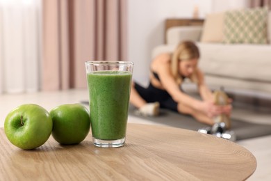 Young woman in fitness clothes doing exercise at home, focus on glass of smoothie and apples