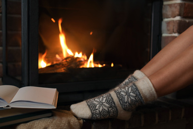 Photo of Woman in knitted socks resting near fireplace at home, closeup. Winter vacation